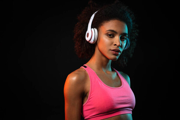 Image of pleased african american woman in headphones looking at camera isolated over black background