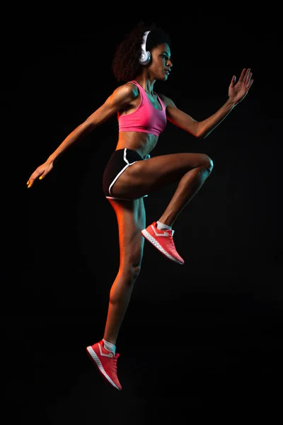 Изображение Сфокусированной Африканской Женщины Наушниках Прыгающей Время Тренировки Черном Фоне — стоковое фото