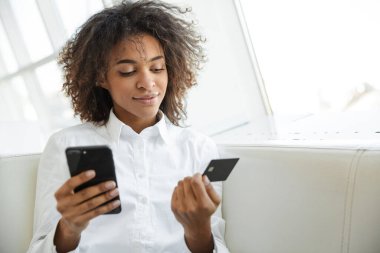 Kafede cep telefonu ve kredi kartı kullanan güzel bir Afrikalı Amerikalı kadının portresi.