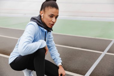 Stadyumda koştuktan sonra kablosuz kulaklık takan çekici Afrikalı genç bir sporcu.