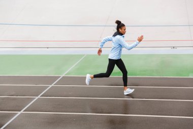 Stadyumda çalışan, kablosuz kulaklık takan, güzel ve formda Afrikalı bir sporcu.