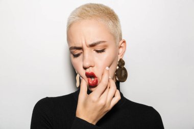 Çekici, genç, seksi, kısa saçlı, küpe takan bir kadının portresi. Beyaz arka planda soyutlanmış, somurtkan.