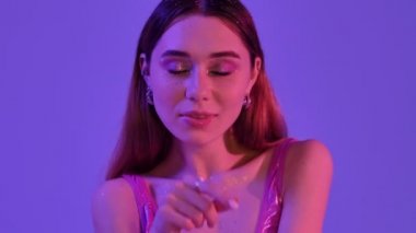 Parlak makyajlı güzel bir moda kadını menekşe neon arkaplanda dudaklarına işaret parmağı tutuyor.