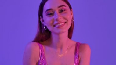 Moda makyajlı oldukça olumlu bir kadın elini menekşe neon arka planda izole bir şekilde sallıyor.