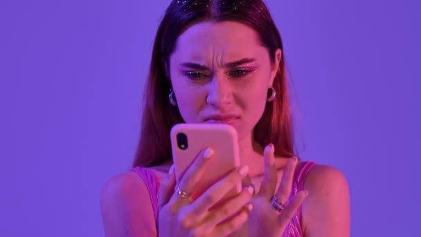 一位穿着时尚艳丽化妆品的不悦女人在手机上发现了一些恶心的东西 这些东西被紫色的霓虹灯背景隔开了 — 图库视频影像