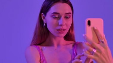 Moda makyajlı neşeli bir kadın menekşe neon arka planında izole edilmiş selfie fotoğrafları çekiyor.