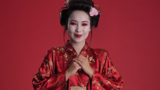 Krásná mladá gejša žena v tradičním japonském kimonu se usmívá stojí izolovaně přes červené pozadí