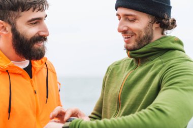 İki kendine güvenen genç sporcu deniz kıyısında işten sonra istirahat ediyor, akıllı bakışlara bakıyor.