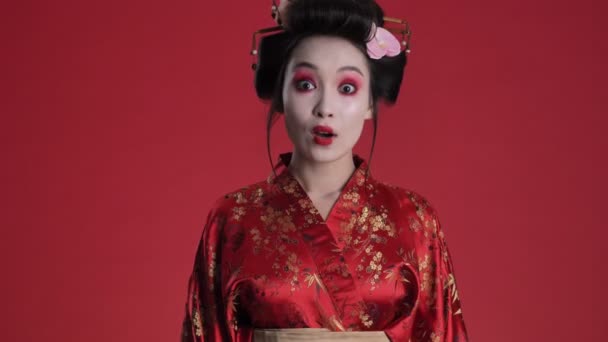 一位穿着日本传统和服 令人惊讶的年轻艺妓站在红色的背景下 感到非常高兴 — 图库视频影像