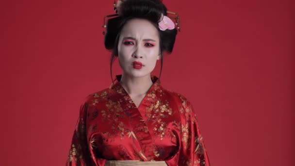 一位身穿日本传统和服的困惑而沮丧的年轻艺妓不同意某种与红色背景隔离的东西 — 图库视频影像