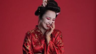 Geleneksel Japon kimonosu giymiş mutlu, genç bir geyşa kırmızı arka planda yalnız bir şekilde gülüyor.