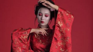 Geleneksel Japon kimonosu giymiş büyüleyici genç bir geyşa kırmızı arka planda tek başına poz veriyor.