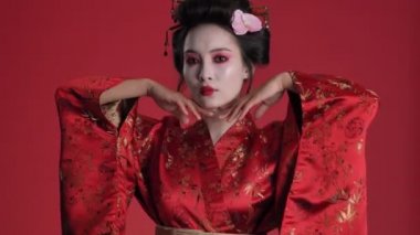 Geleneksel Japon kimonosu giymiş harika bir genç geyşa kırmızı arka planda yalnız bir şekilde poz veriyor.