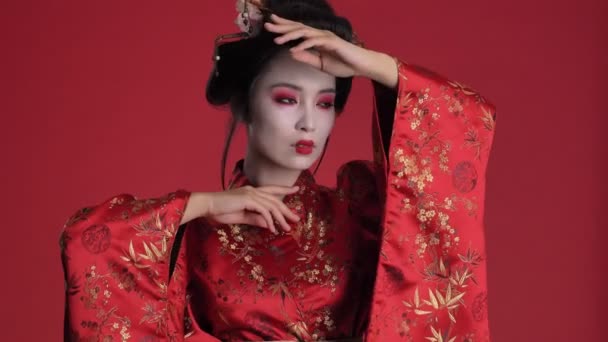 日本の伝統的な着物を着た魅力的な豪華な若い芸者女性が 赤い背景に隔離されたままポーズをとっています — ストック動画