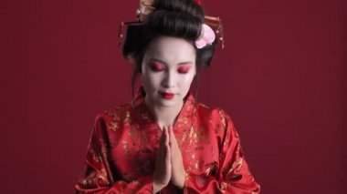Geleneksel Japon kimonolu çekici genç bir geyşa kırmızı arka planda geleneksel Japon selamlaması yapıyor.