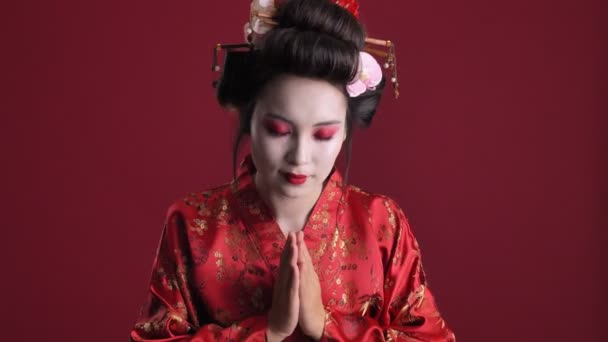 一位穿着日本传统和服的年轻漂亮的艺妓正在做着传统的日语问候 与红色背景隔离开来 — 图库视频影像