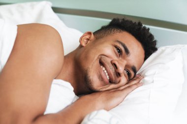 Mutlu, pozitif gülümseyen Afrikalı genç bir adamın sabah yatak odasında yatışı..