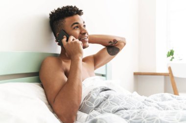 Sabah yatak odasında cep telefonuyla konuşan mutlu, Afrikalı bir genç resmi..