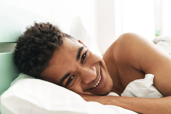 一个快乐而积极的笑着的年轻非洲小伙子早上躺在卧室的照片躺在床上 — 图库照片
