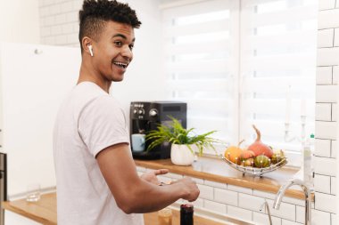 Genç Afrikalı pozitifin sabah mutfakta kahvaltı hazırlarken çekilmiş fotoğrafı. Kulaklıklı tatlı reçelli sandviçler yapıyor..