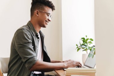 Genç, mutlu, gülümseyen Afrikalı bir adamın sabah bilgisayarı kullanırken fotoğrafı..