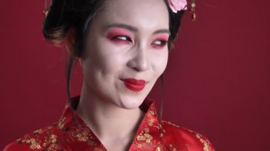 Geleneksel Japon kimonolu oldukça hoş genç bir geyşanın yakın plan görüntüsü kırmızı arkaplanda izole edilmiş kameraya bakıyor.