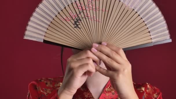 日本の伝統的な着物に身を包んだ若い芸者衆の姿が 赤い背景に孤立した表情を変えながら 扇面から間近に描かれている — ストック動画