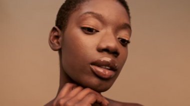 Şehvetli, yarı çıplak, kısa siyah saçlı ve bej arka planda gezinen Afrikalı bir kadının yakın görüntüsü.