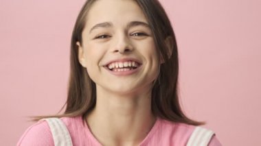 Tulum giymiş, pembe arka plan üzerinden kameraya bakan neşeli, esmer kadının yakın görüntüsü.
