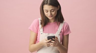 Tulum giyen, akıllı telefon kullanan ve pembe arka plan için üzülen mutlu esmer kadın.