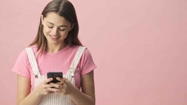 Glückliche Hübsche Brünette Frau Overalls Mit Smartphone Über Rosa Hintergrund — Stockvideo