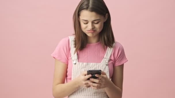 不満かなりブルネット女性で全体的に使用してスマートフォン以上ピンクの背景 — ストック動画