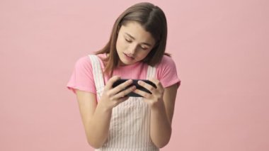 Tulumlu, pembe arka planda akıllı telefonla oynayan esmer, üzgün bir kadın.