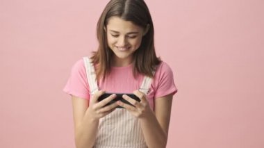 Tulum giymiş güzel, esmer bir kadın akıllı telefonuyla oynuyor ve pembe arka plan için üzülüyor.