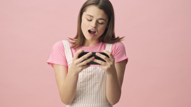 Verwarde Mooie Brunette Vrouw Overalls Spelen Smartphone Roze Achtergrond — Stockvideo