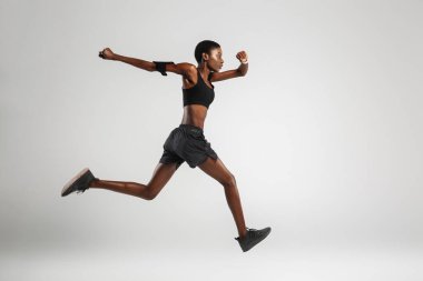 Beyaz arka planda izole bir şekilde çalışırken cep telefonu ve kulaklık kullanan Afro-Amerikan kadın görüntüsü