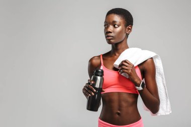 Beyaz arka planda izole bir şekilde çalışırken havluyla su içen Afrikalı Amerikalı sporcu.
