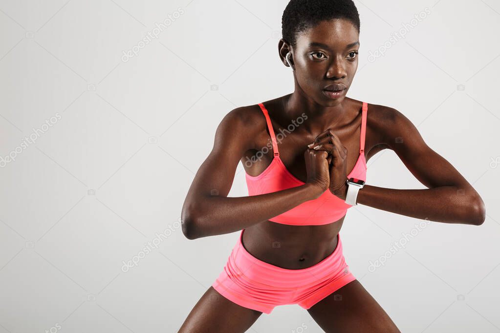 Image of african american sportswoman using wireless earbuds while working out isolated over white background