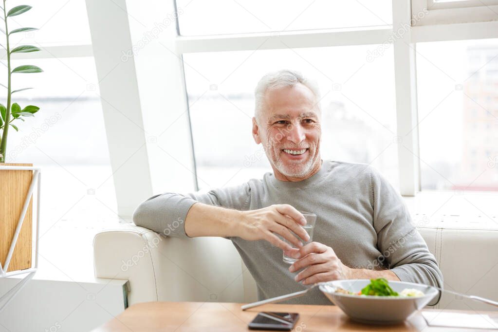 Picture of a mature happy smiling senior grey-haired bearded businessman sit in cafe have a dinner.