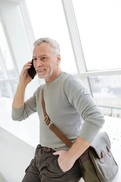 Photo Handsome Mature Man Smiling Talking Cellphone While Standing Windows — Stock Photo, Image