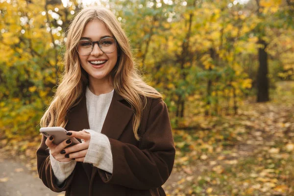 Gyönyörű Fiatal Vidám Kabátban Sétál Őszi Parkban Mobiltelefonnal — Stock Fotó