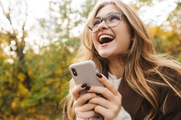 Gyönyörű Fiatal Vidám Kabátban Sétál Őszi Parkban Mobiltelefont Használ Nevet — Stock Fotó