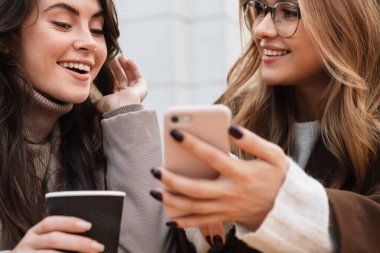 Kafede oturup kahve içerken cep telefonuna bakan iki neşeli ve çekici bayan arkadaşa yakın durun.