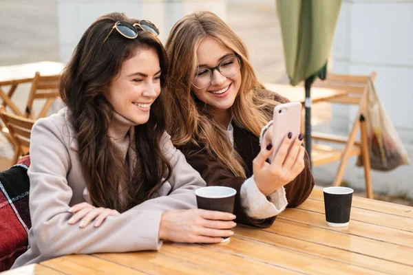 Dvě Veselé Atraktivní Ženy Přátelé Sedí Kavárně Venku Dívá Mobilní — Stock fotografie