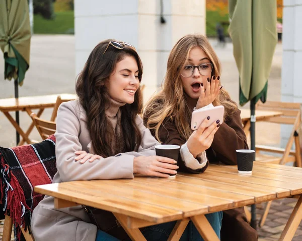 Két Vidám Vonzó Barátok Kávézóban Szabadban Nézi Mobiltelefon Miközben Iszik — Stock Fotó