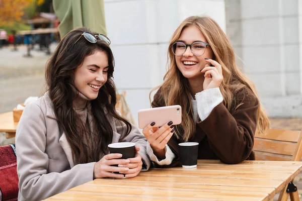 Két Vidám Vonzó Barátok Kávézóban Szabadban Nézi Mobiltelefon Miközben Iszik — Stock Fotó