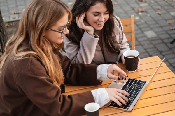 两个快乐迷人的女性朋友坐在外面的咖啡馆里 在笔记本电脑上工作 — 图库照片