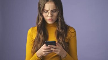 Hoşnutsuz bir genç kız telefonuyla sohbet ediyor. Stüdyonun mor arka planında tek başına dikiliyor.