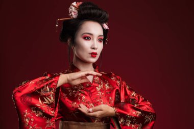 Geleneksel Japon kimonosu giymiş Asyalı genç bir geyşanın kırmızı arka planda yalnız dans edişi.