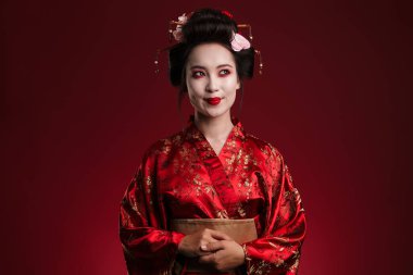 Kırmızı arka planda izole edilmiş geleneksel Japon kimonolu güzel genç bir geyşa resmi.